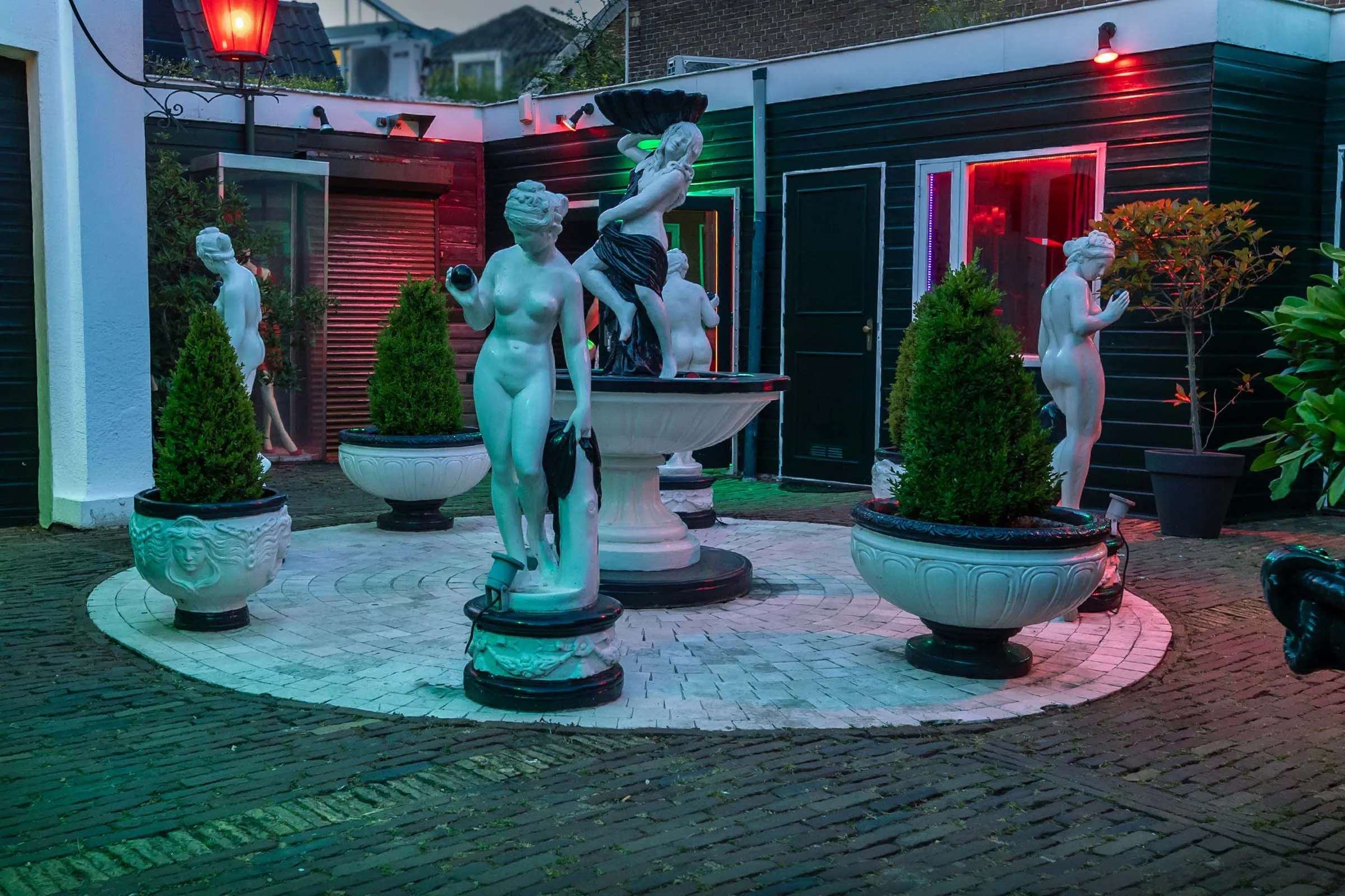 De binnenplaats van het hofje in de avond, met beelden rond een fontein.